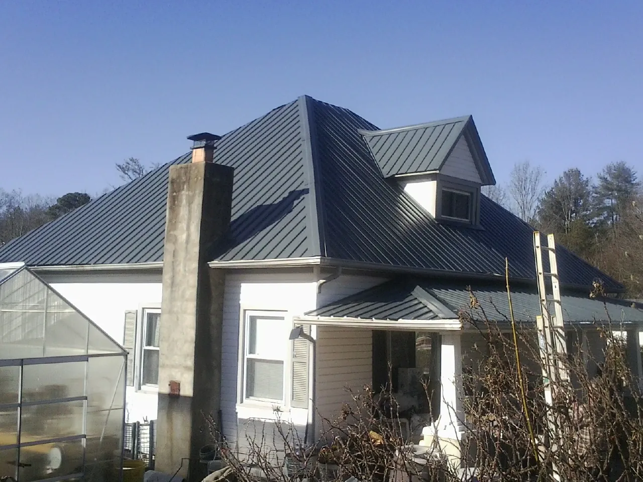 Dark blue standing seam metal roof on a white farmhouse with dormer — Slate & Tile Roof Repair by Roofing Brothers in Welcome