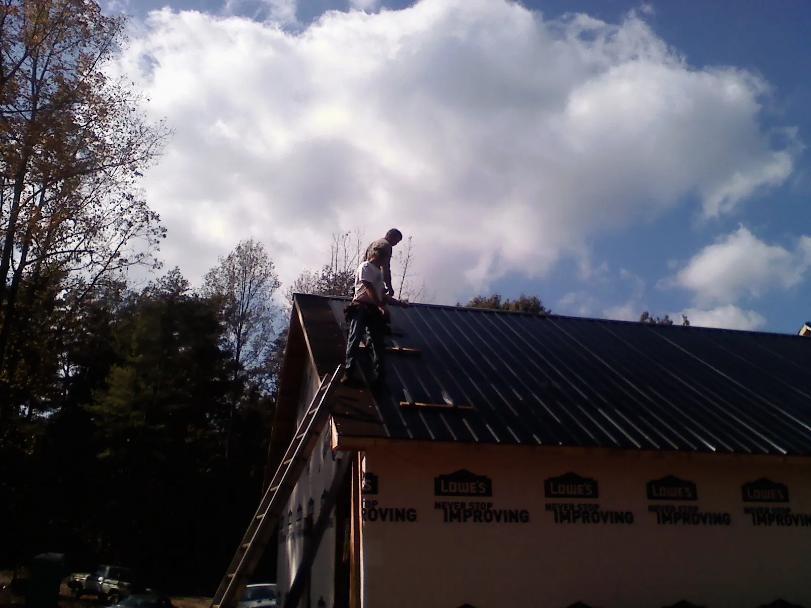 Roofer fastening dark metal panels high against a cloudy sky, from a Roof Inspection job in Welcome